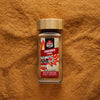Ceylon Cinnamon powder in a glass spice jar with single-origin ground Cinnamon scattered in the background