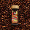Whole Sri Lankan cloves in a glass spice jar with loose cloves scattered in the background